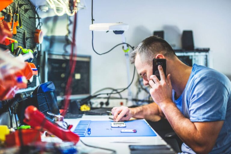 man speaking on mobile phone repairing electronics in service shop 1024x683 1